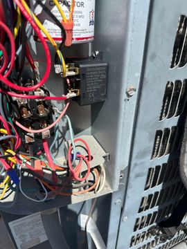 Open electrical control panel with tangled red, black, and blue wires and circuit components.