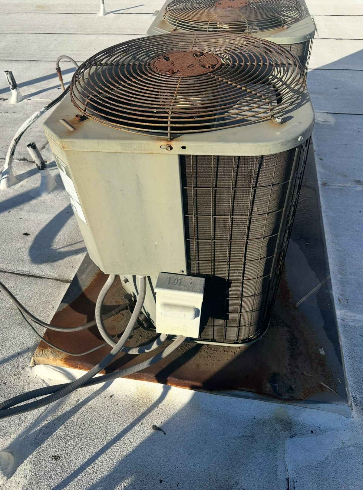 Two air conditioning units on a white roof, weathered with rust and dirt.