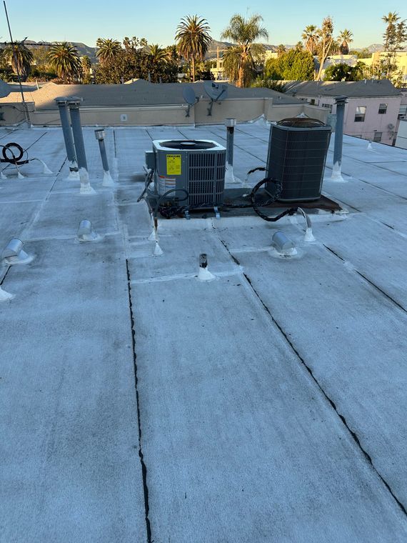 Rooftop HVAC unit with ductwork on a flat white roof at sunset.