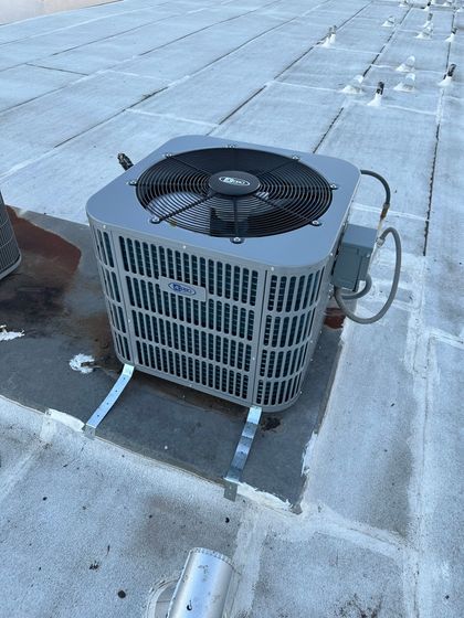 Outdoor HVAC unit on a flat rooftop with a black fan grille and metal sides, surrounded by snow patches.