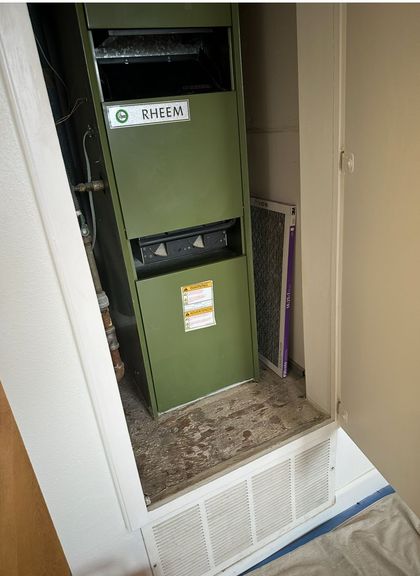 Green HVAC unit in a closet with open access panel and white vent grille below