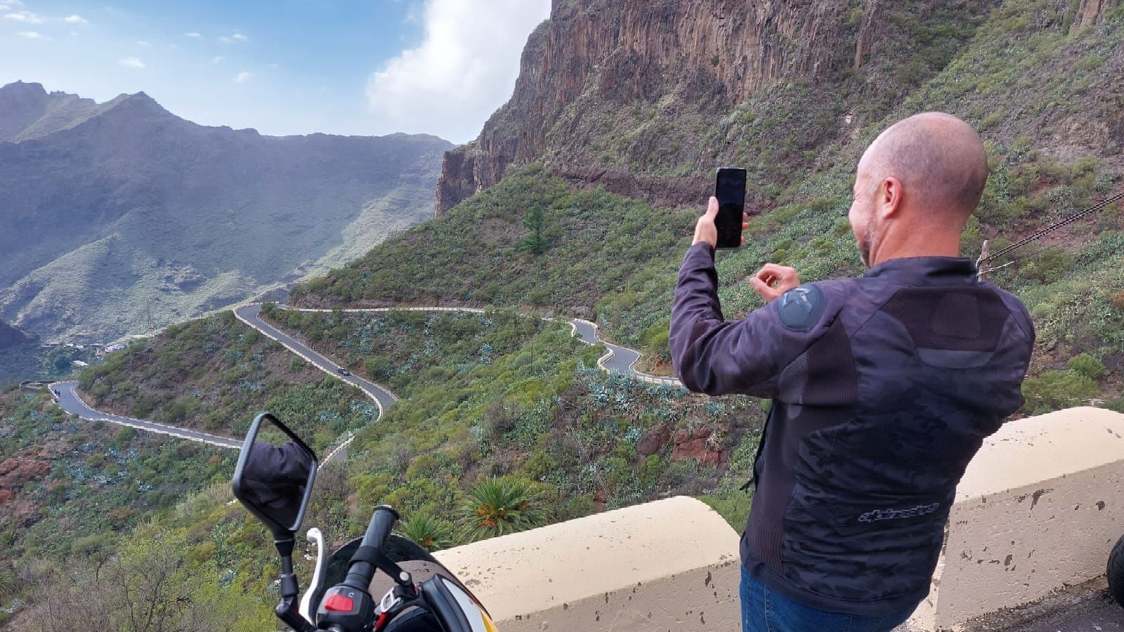 A man is taking a picture of a mountain with his cell phone.