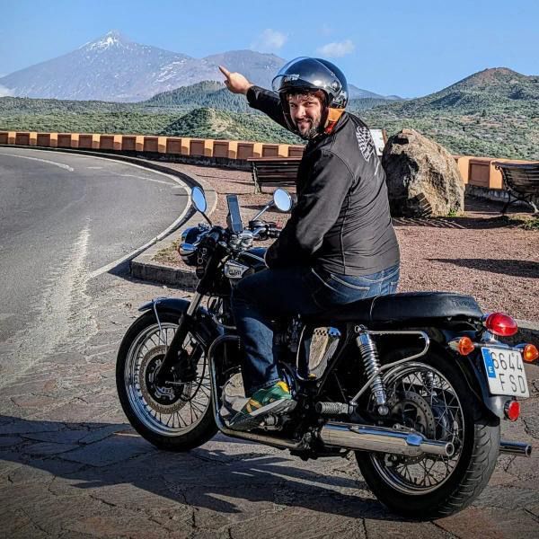 A man is riding a motorcycle down a road with mountains in the background.