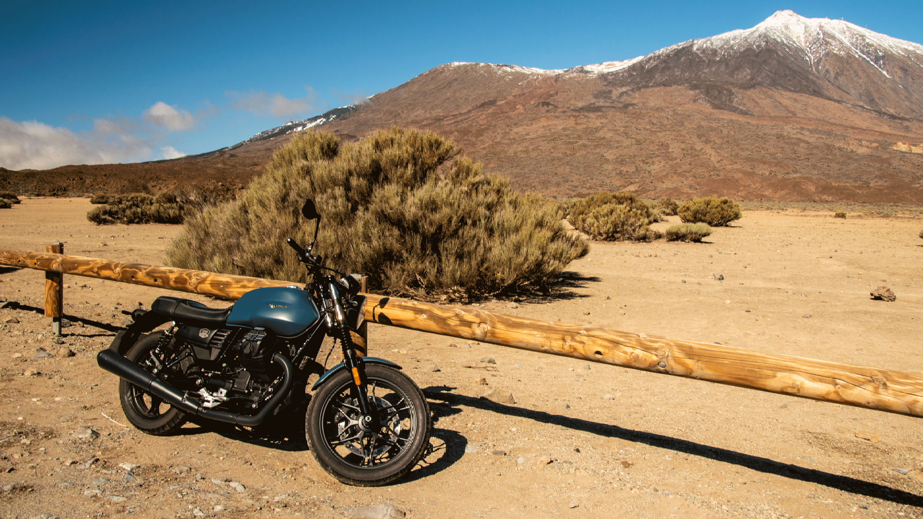 A motorcycle is parked in the desert in front of a mountain.