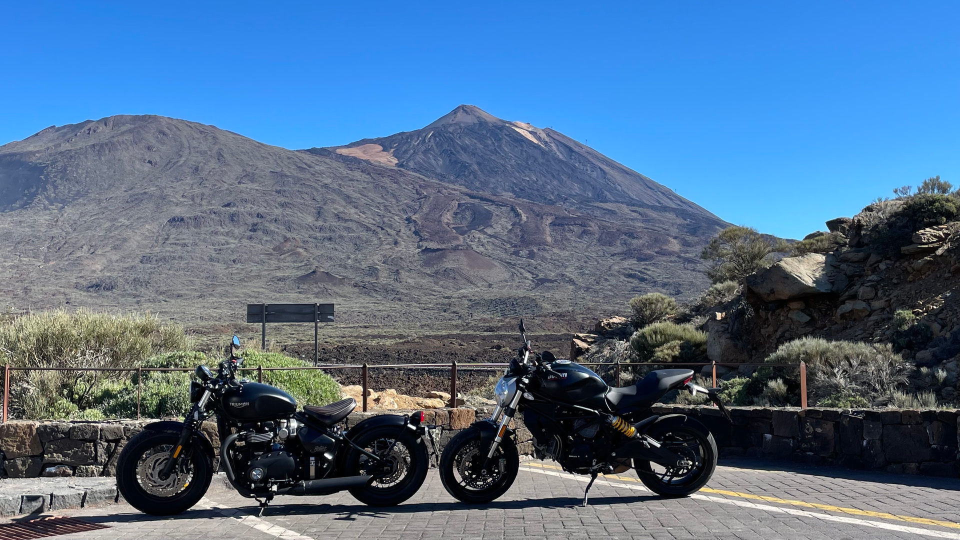 Two motorcycles are parked on the side of a road with a mountain in the background