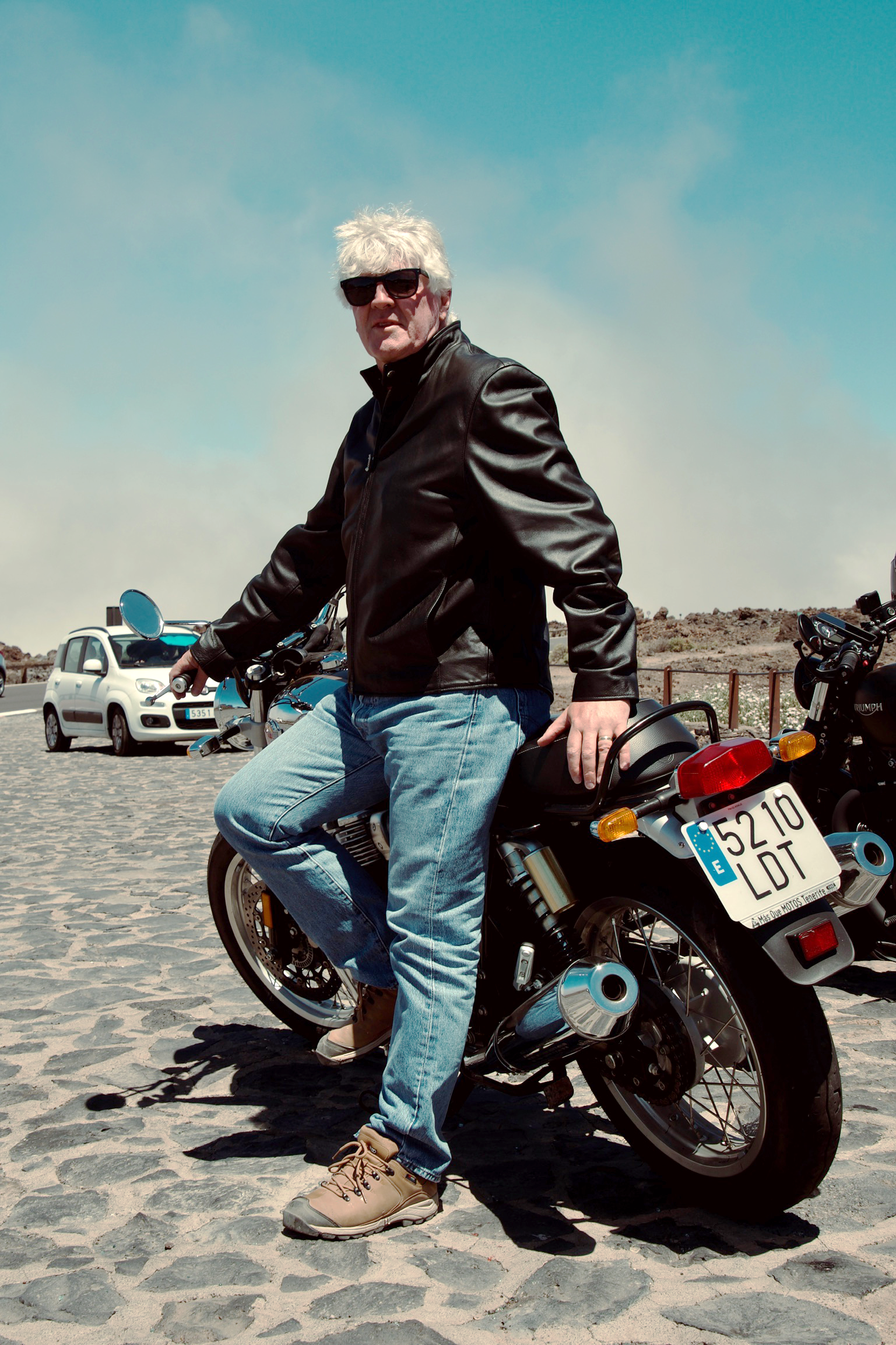 A man is leaning on a motorcycle on a cobblestone street.