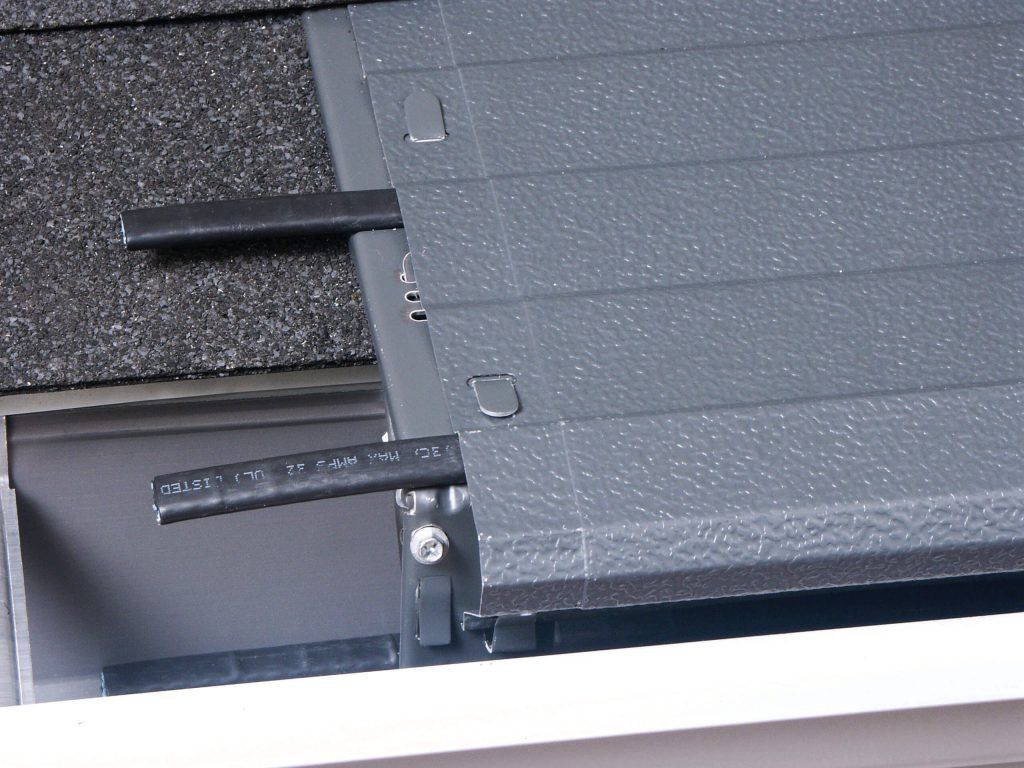 A gray gutter guard system installed on a roof edge, showing mounting hardware and a textured surface.