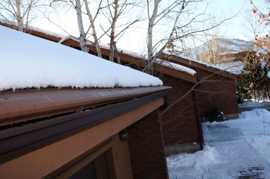 A close-up view of a brown gutter on a brick building, covered with a thick layer of snow during winter.