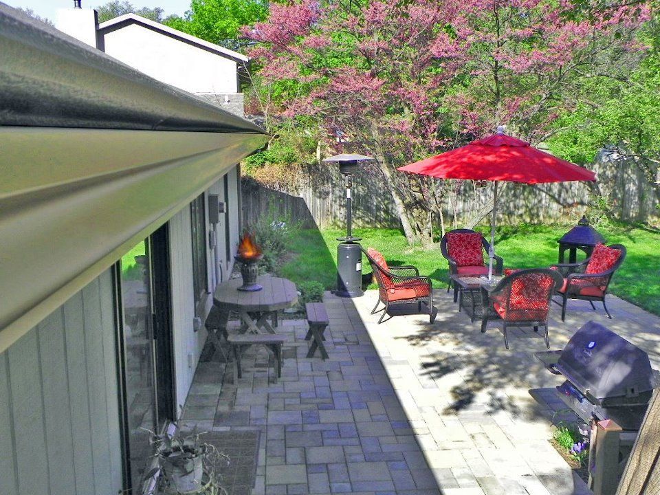 A sunny outdoor patio with a red umbrella, seating, a grill, and a heater, viewed from above near the house roofline.