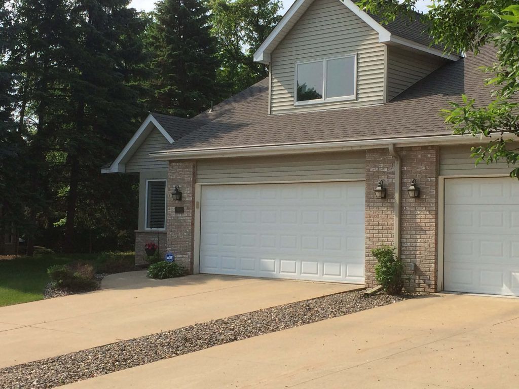 A tan house with a brick facade and two white garage doors, featuring a pebble strip running through the concrete driveway.
