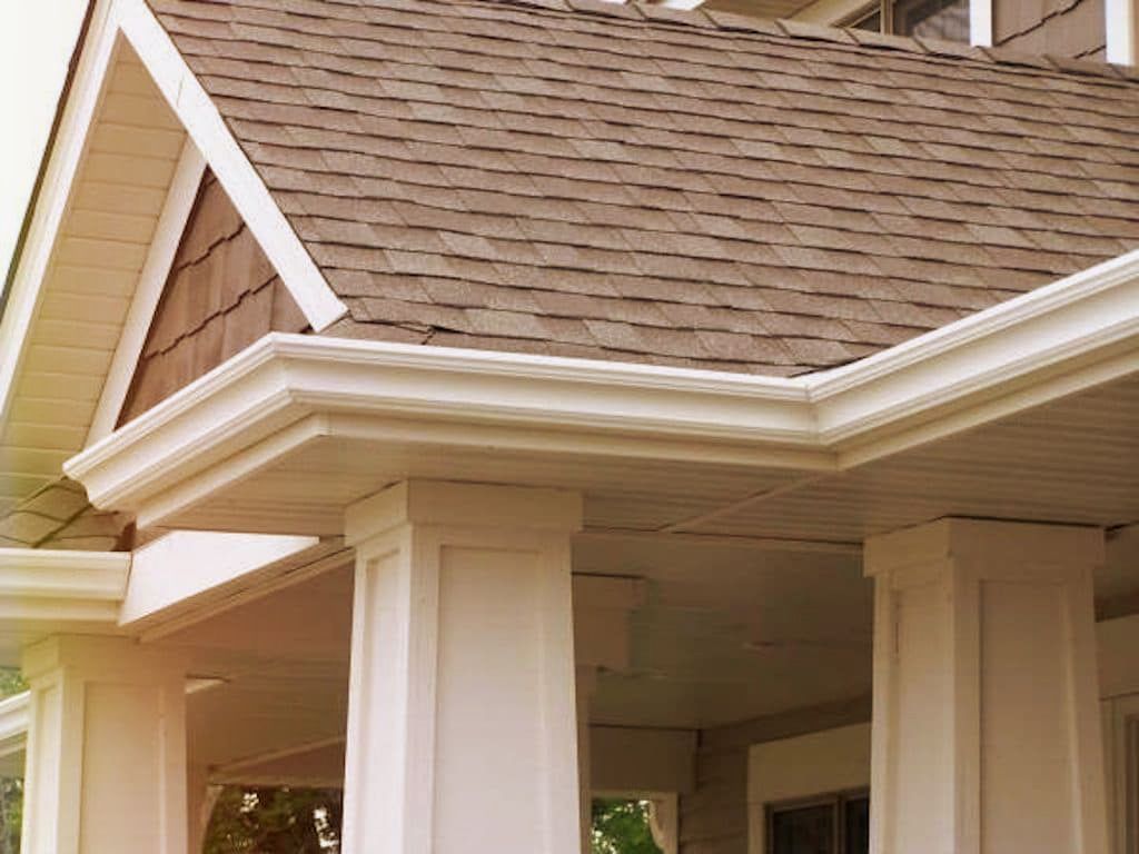 A brown shingled roof with white gutters and trim supported by two large, white porch columns.