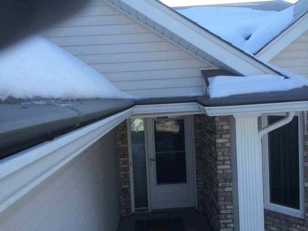 A residential home entryway with cream siding and brick accents, featuring snow-covered gutters and a covered porch door.