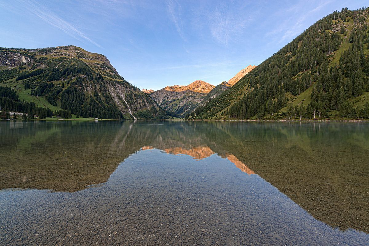 Kristallklarer Bergsee Vilsalpsee in den Alpen mit perfekter Spiegelung der Berge und Kieselboden im Vordergrund.