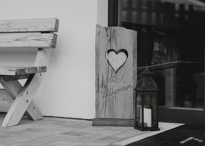 Rustikales Holzschild mit Herz und Willkommen-Schriftzug neben Laterne und Holzbank am Eingang