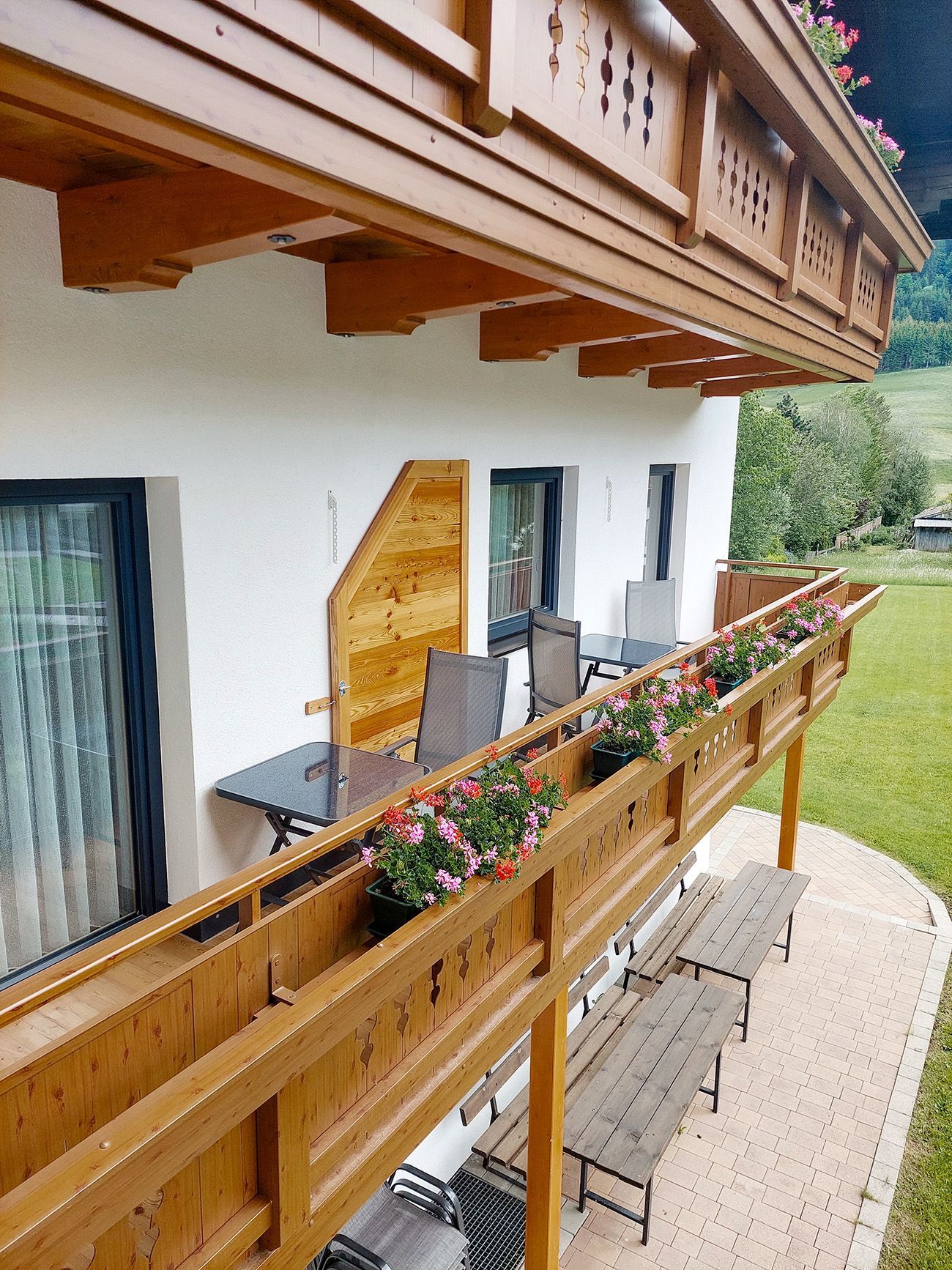 Holzbalkon einer Ferienunterkunft mit blühenden Blumenkästen und gemütlichen Sitzgruppen.