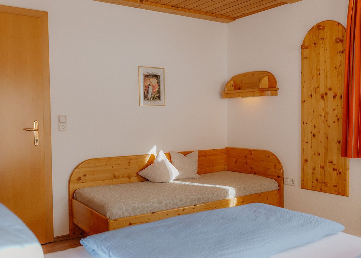 Helles Zimmermit einer rustikalen Holzdecke, einemTagesbett in der Ecke und einem Doppelbett mit hellblauer Bettwäsche