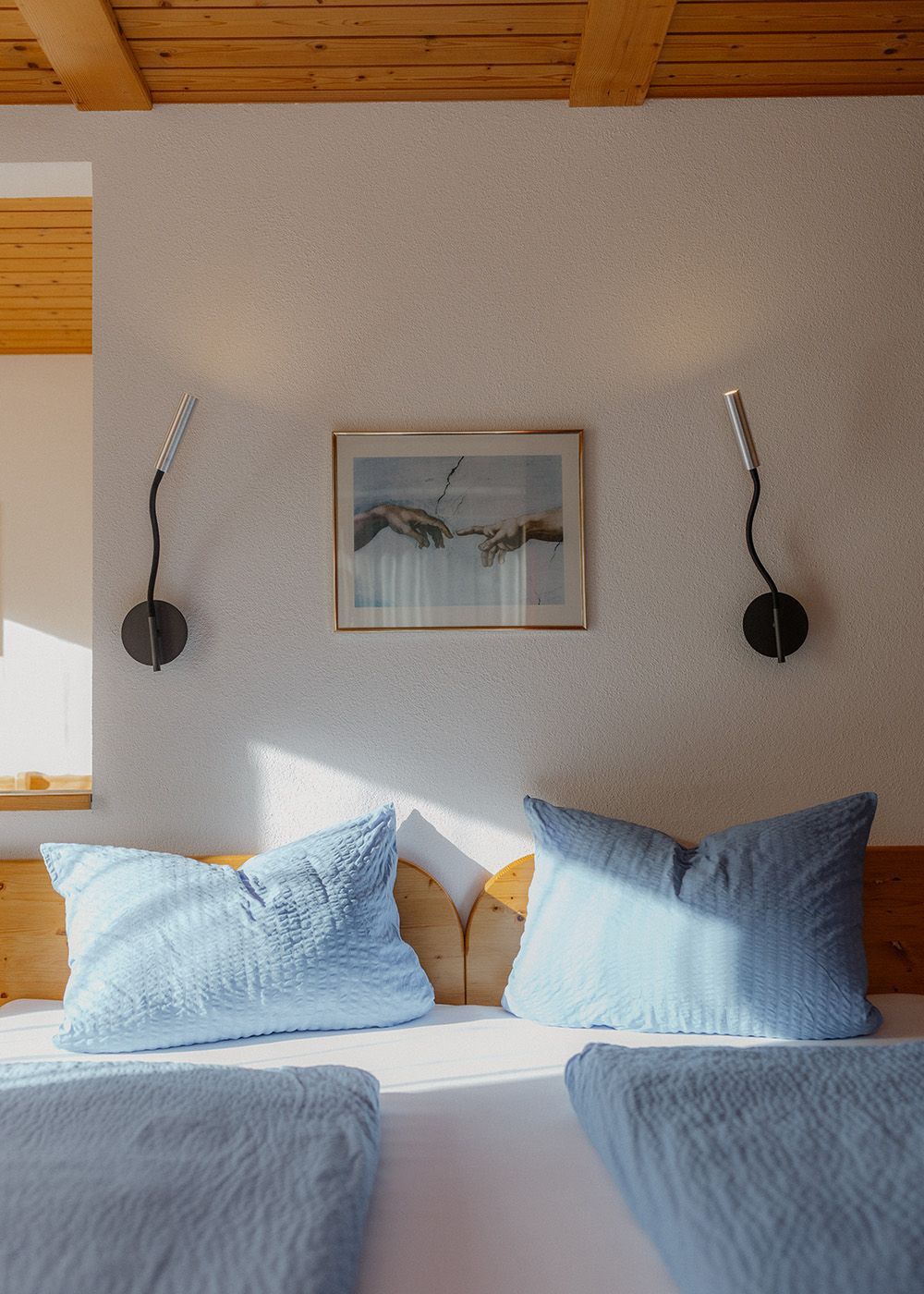 Gemütliches Doppelbett mit hellblauer Bettwäsche, modernen schwarzen Wandleseleuchten und einem gerahmten Kunstbild.