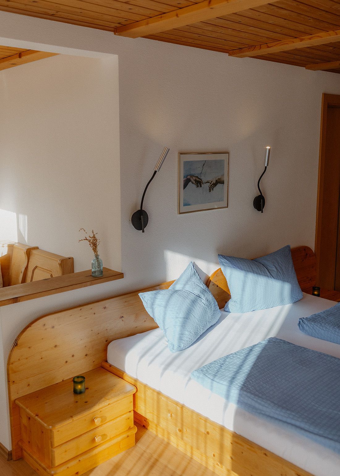 Gemütliches Doppelbett mit hellblauer Bettwäsche, modernen schwarzen Wandleseleuchten und einem gerahmten Kunstbild.