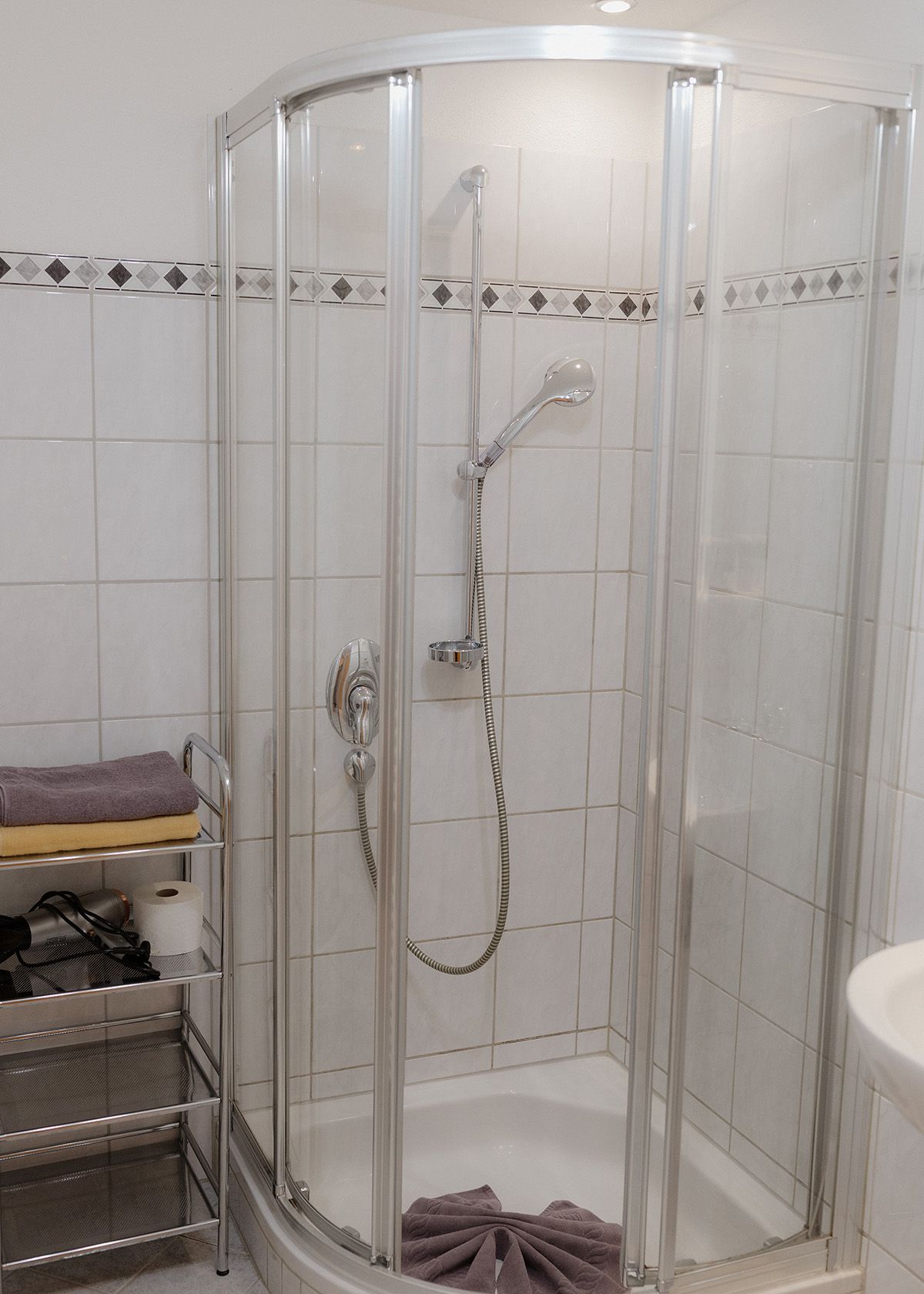 Hell gefliestes Badezimmer mit einer modernen Runddusche aus Glas und einem weißen Waschbecken mit verchromten Armaturen.