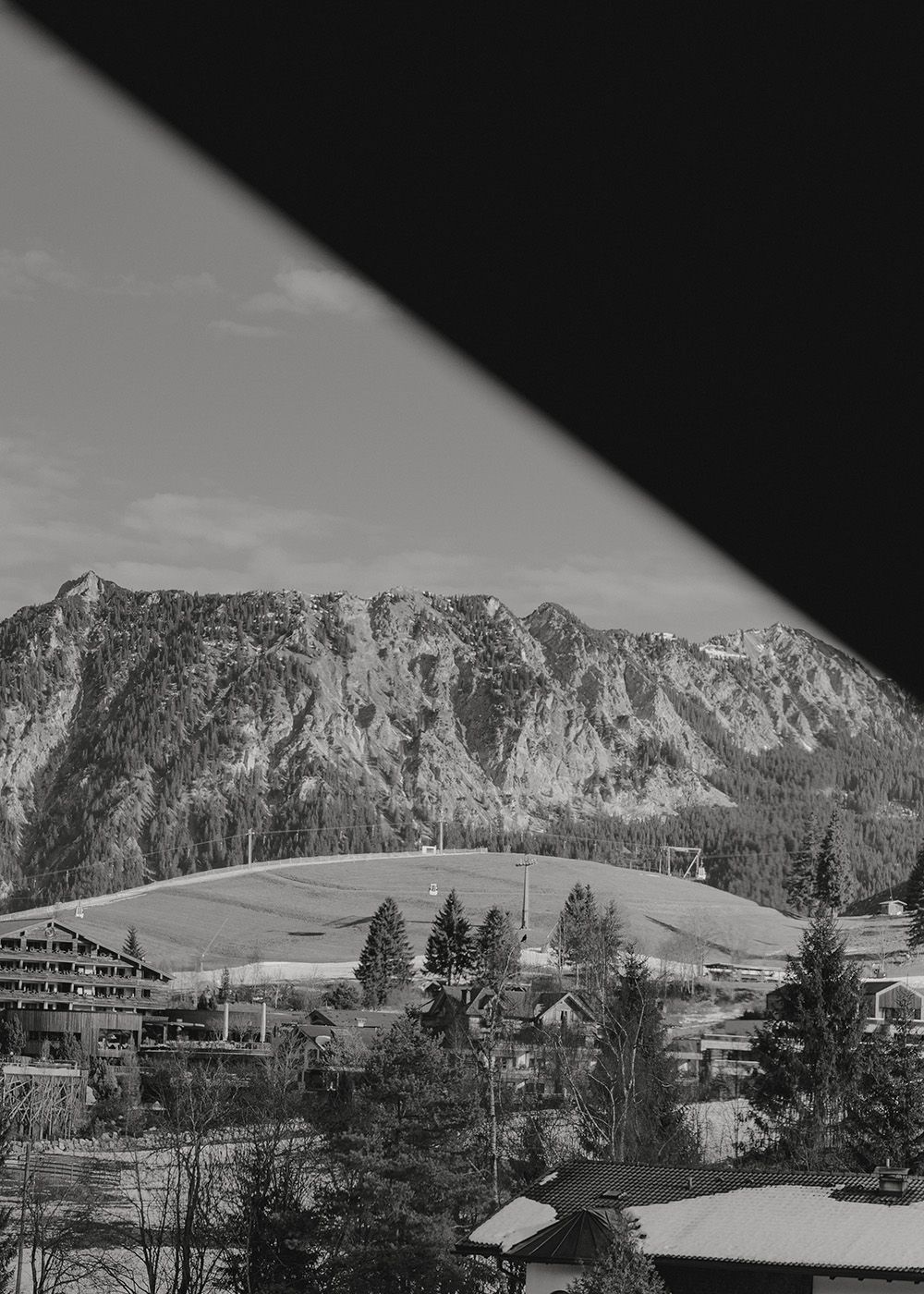 Blick auf ein Hotel mit Seilbahn und imposanter Bergkulisse in Schwarz-Weiß.