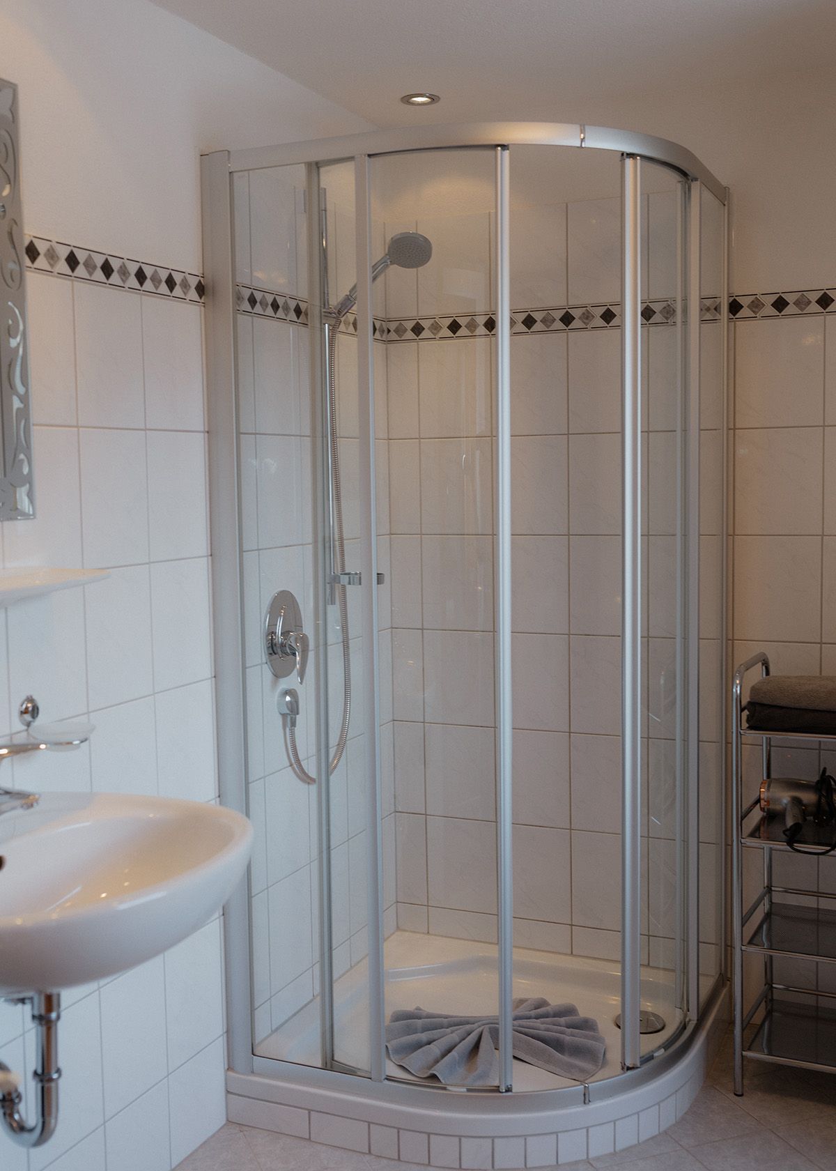 Hell gefliestes Badezimmer mit einer modernen Runddusche aus Glas und einem weißen Waschbecken mit verchromten Armaturen.