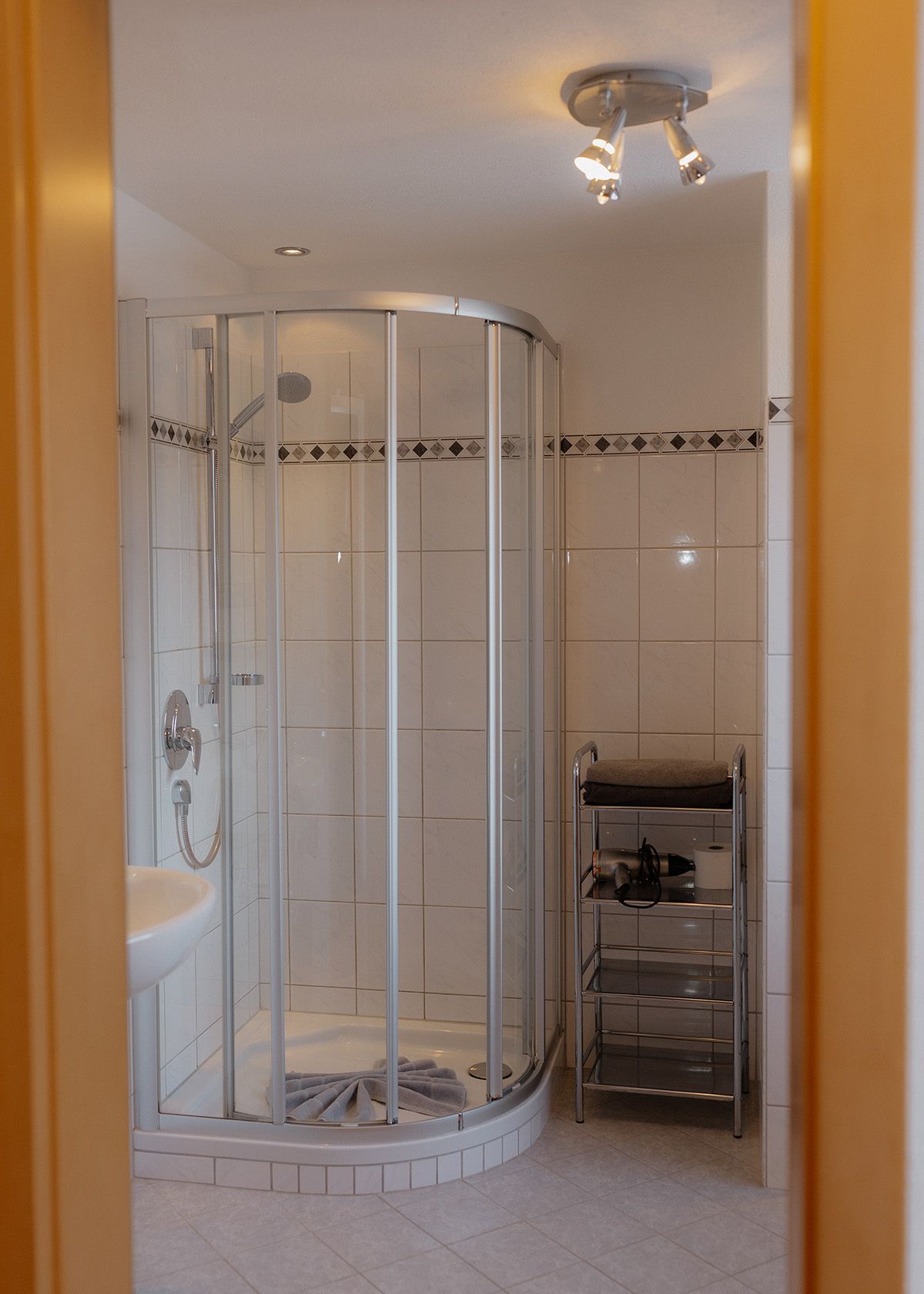 Hell gefliestes Badezimmer mit einer modernen Runddusche aus Glas und einem weißen Waschbecken mit verchromten Armaturen.