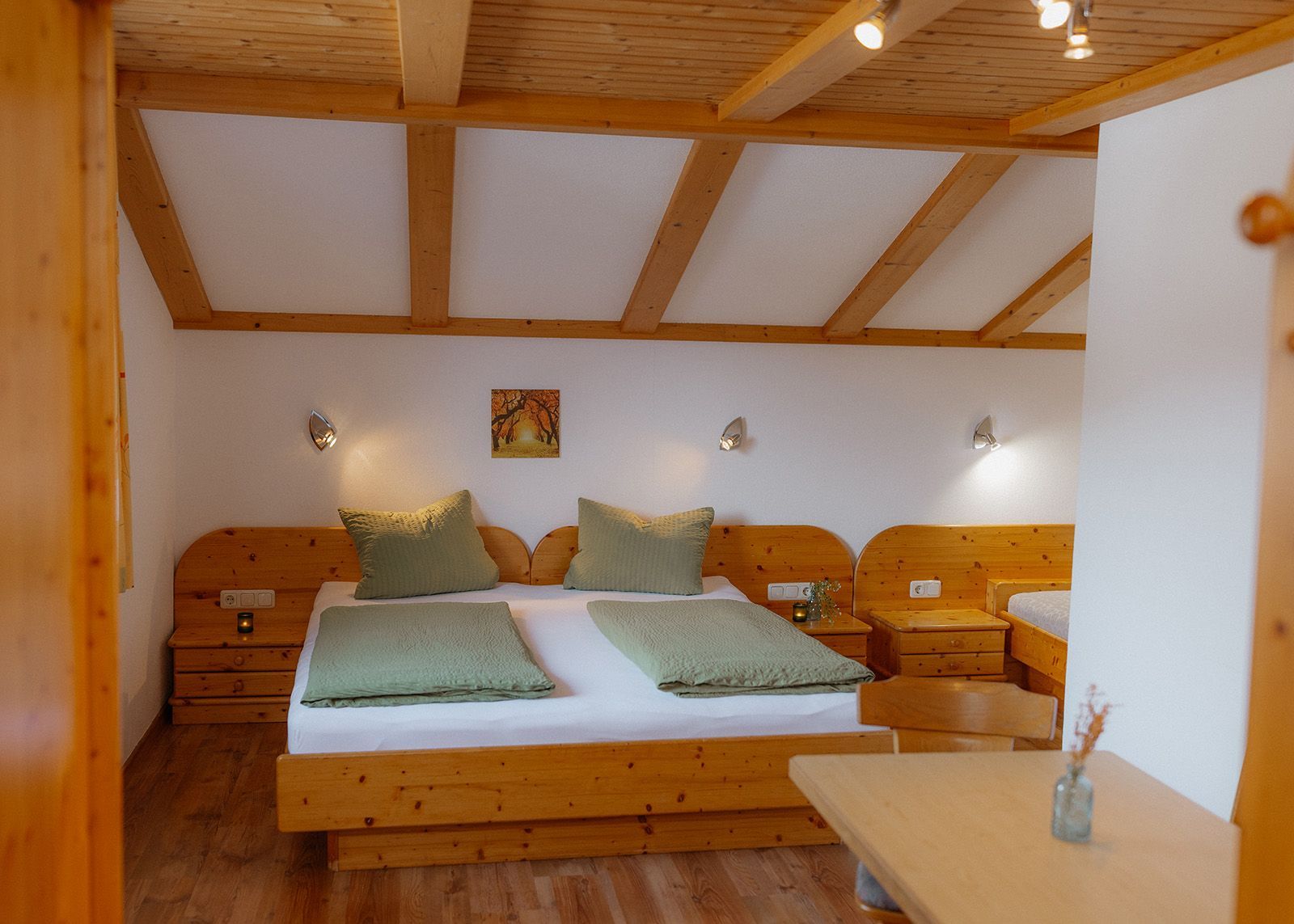 Gemütliches Schlafzimmer einer Ferienwohnung mit Holz-Doppelbett, grüner Bettwäsche und Holzbalkendecke.