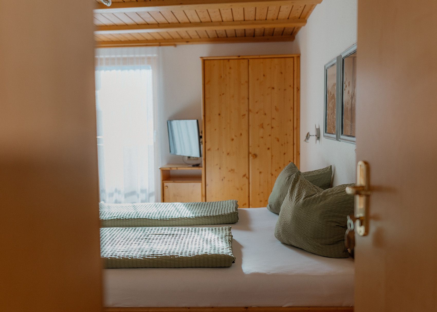 Gemütliches Schlafzimmer einer Ferienwohnung mit Holz-Doppelbett, grüner Bettwäsche und Holzbalkendecke.