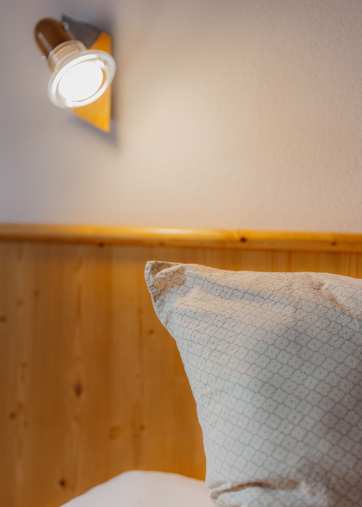 Gemütliches Bett mit Kissen, leuchtender Wandlampe und heller Holzverkleidung im Schlafzimmer.