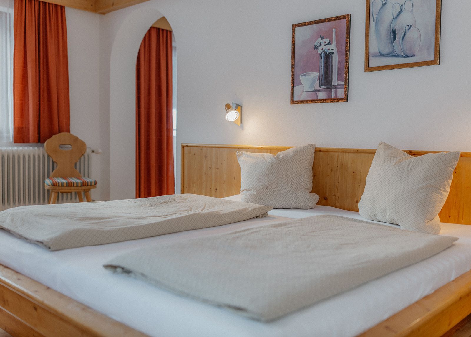 Gemütliches Bett mit Kissen, leuchtender Wandlampe und heller Holzverkleidung im Schlafzimmer.