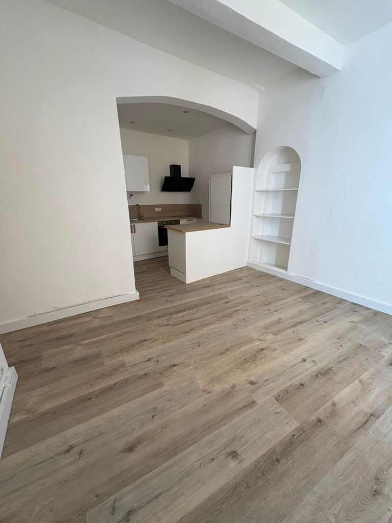 Vue intérieure : parquet clair, murs blancs, cuisine avec arche, étagères intégrées.