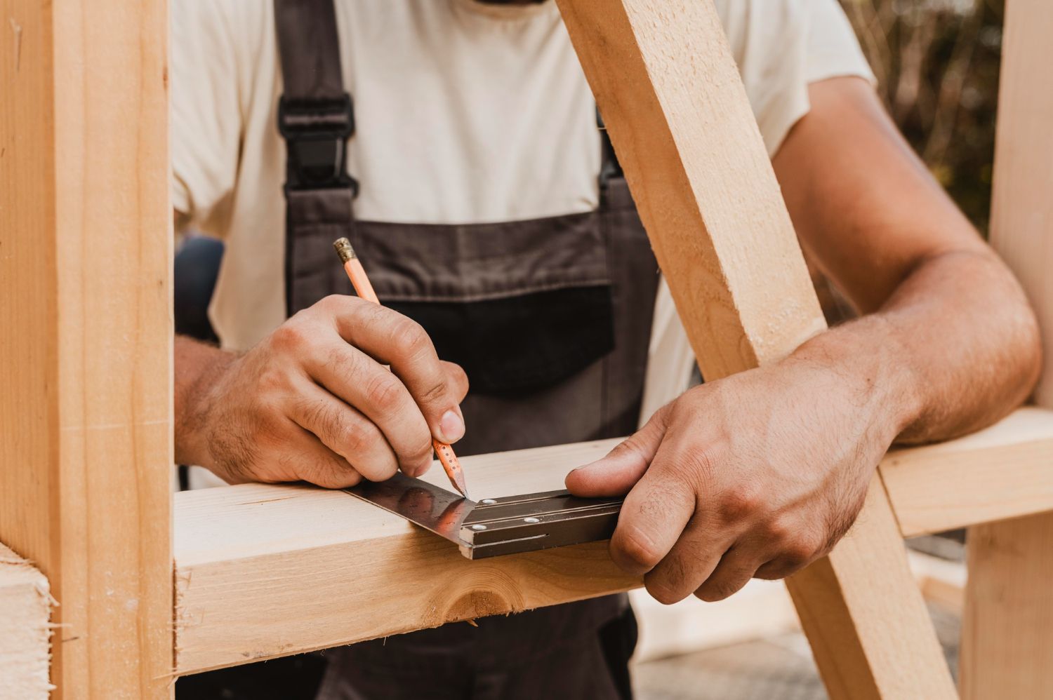 Un charpentier trace des marques sur du bois au crayon et à l'équerre, vêtu d'une salopette.