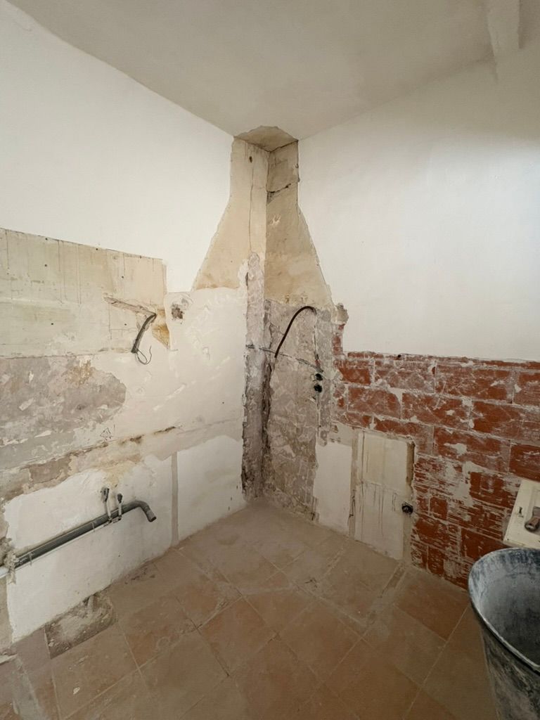 Rénovation de la cuisine en cours : briques apparentes, murs en plâtre, câblage électrique et plomberie visibles.