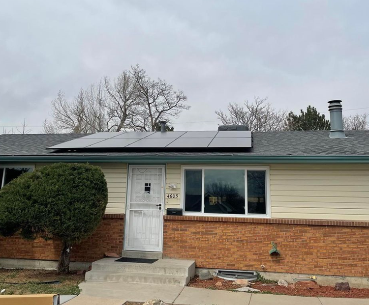 A house with solar panels on the roof and a tree in front of it.