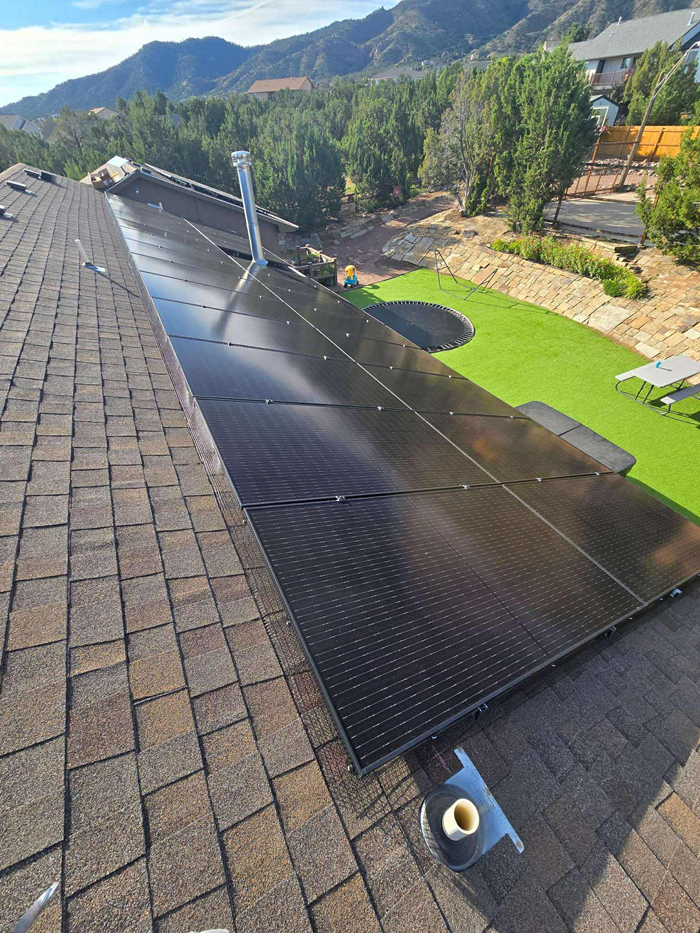 Solar panels installed on a brown shingled roof with a mountain backdrop.