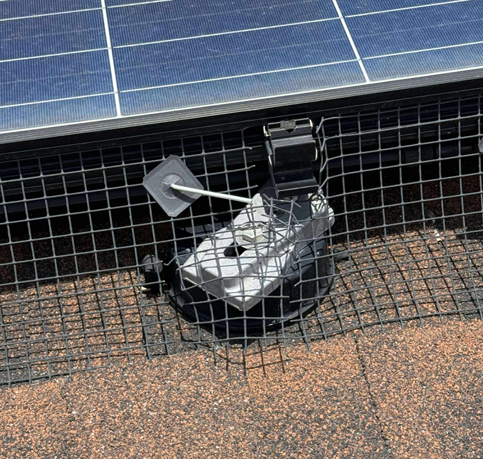 Solar panel bird deterrent: Wire mesh netting installed under the panels, secured by a bracket on a shingled roof.
