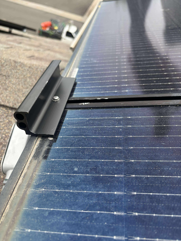 Solar panel on a roof with a black mounting rail and bracket.