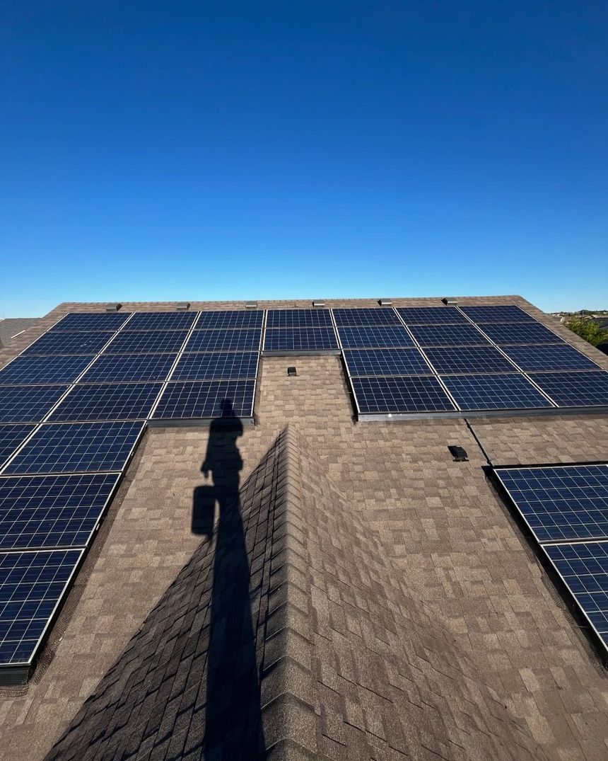 A person is standing on top of a roof with solar panels on it.