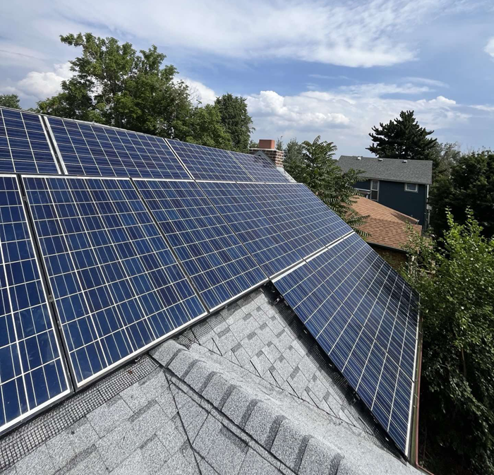Solar panels on a residential roof against a cloudy blue sky.
