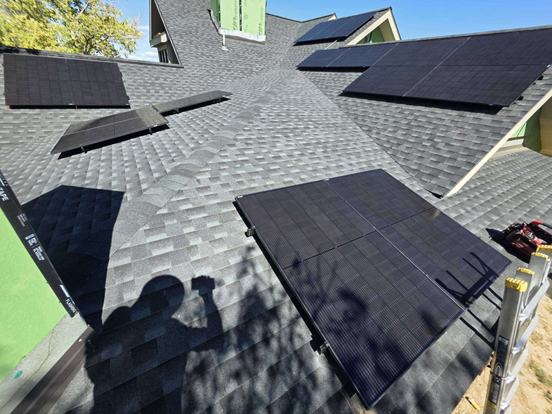 Solar panels installed on a gray shingled roof, with a shadow of a person nearby.