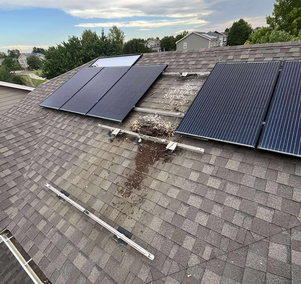 Solar panels on a shingled roof with a debris pile and damaged mounting rails. Cloudy sky.