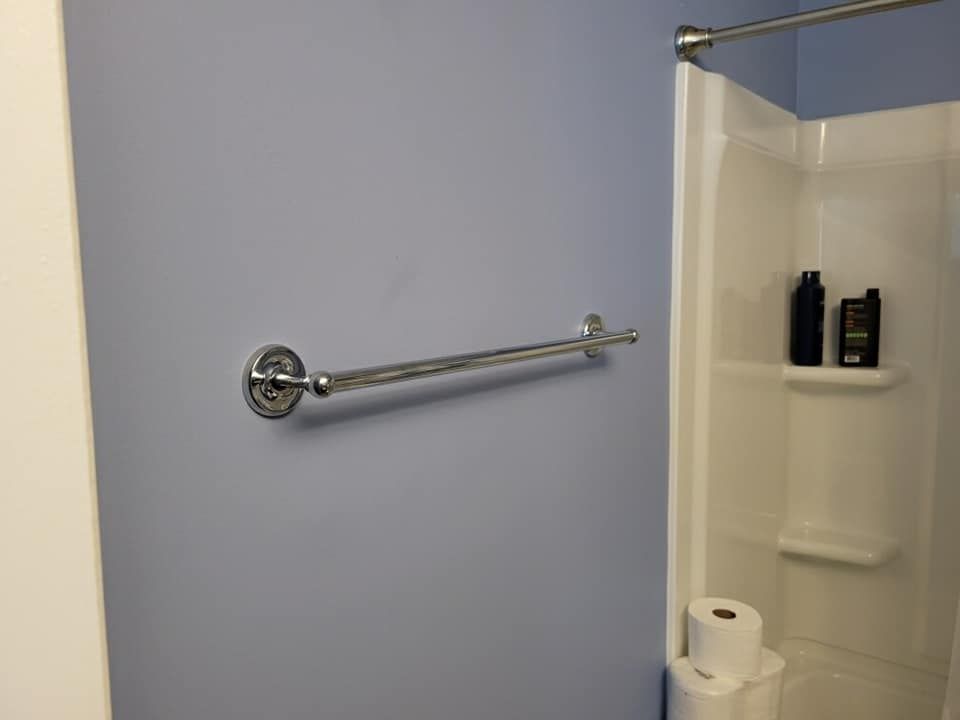 Chrome towel rack on a light blue bathroom wall, next to a white shower stall with toiletries and toilet paper.