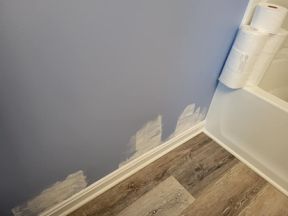 Blue bathroom wall with unfinished paint, white baseboard, and rolls of toilet paper by the tub.