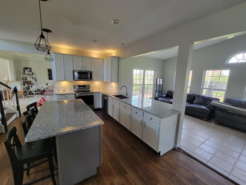 Kitchen with light grey cabinets, granite countertops, and wooden floors; opens to living area with sofas.