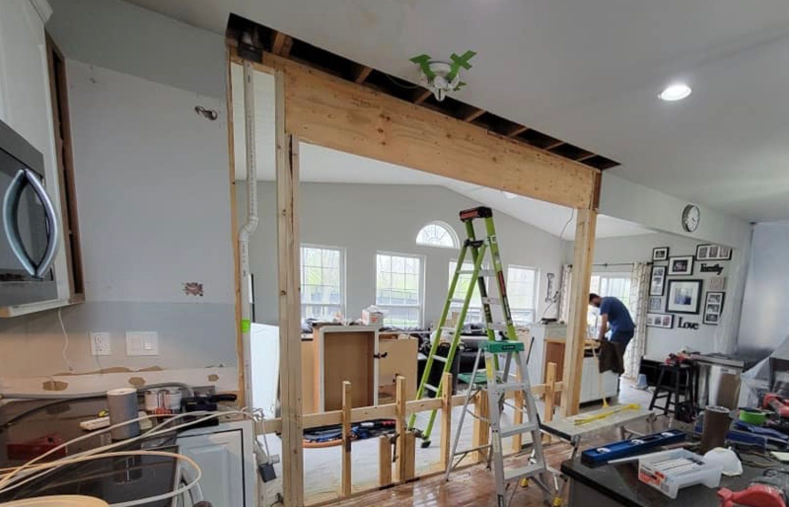 Kitchen undergoing renovation; opening in wall framed with wood; person on ladder.
