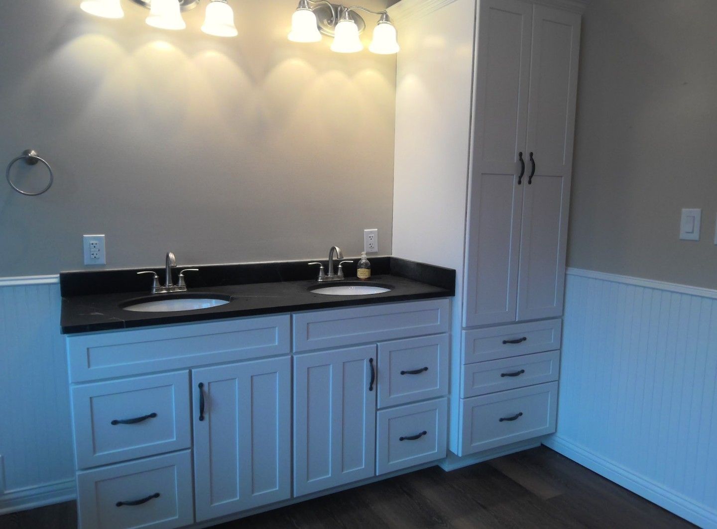 Bathroom with white vanity, black countertop, and tall cabinet; gray walls, beadboard trim.