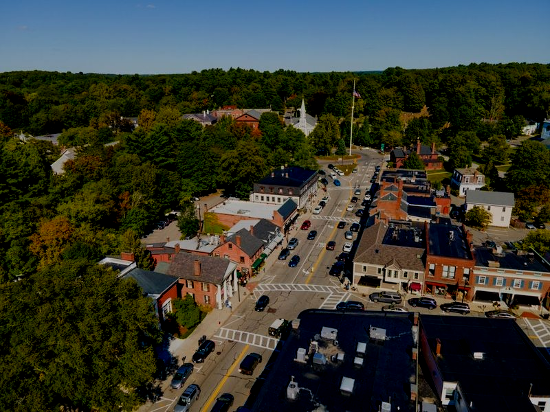 Aerial view of a small town main street with cars, brick buildings, and trees under a clear blue sky