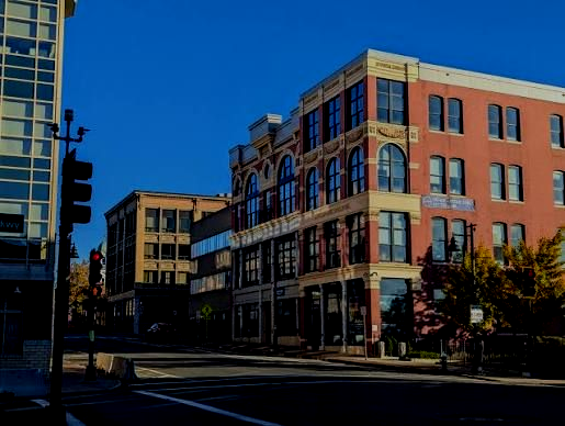 Urban street with brick buildings, storefronts, and a clear blue sky at a city intersection.