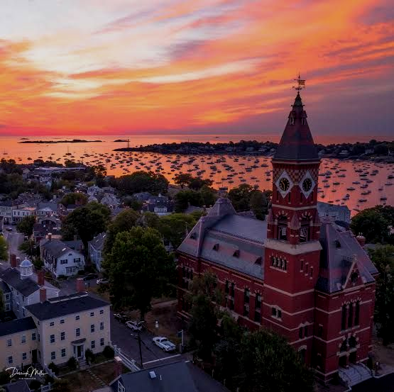 Sunset over a coastal town with a red clock tower and boats on calm water