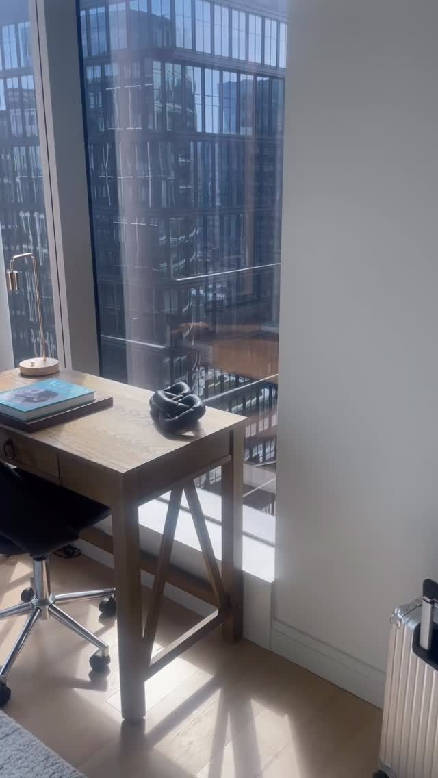 Desk by a window with a swivel chair, overlooking tall office buildings in daylight.